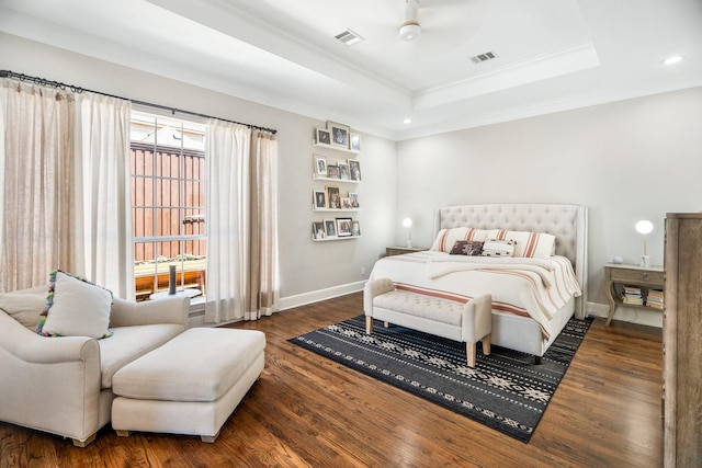 bedroom featuring wood finished floors, ornamental molding, baseboards, visible vents, and a raised ceiling