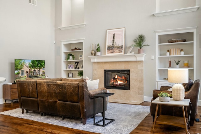 living room with a towering ceiling, wood finished floors, visible vents, and built in shelves