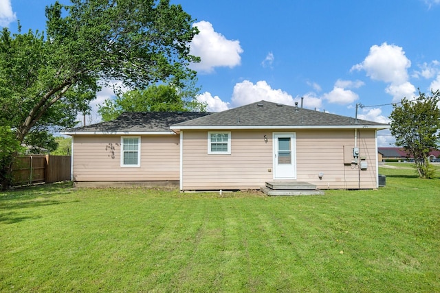 back of property with fence, a yard, and roof with shingles