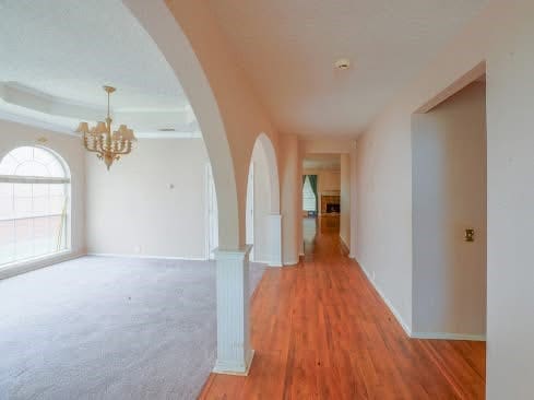 corridor with arched walkways, baseboards, a chandelier, and light wood-type flooring