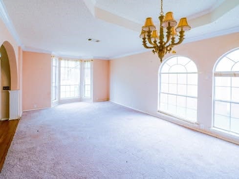 unfurnished room featuring an inviting chandelier, carpet floors, crown molding, and arched walkways