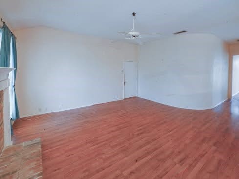 empty room featuring a fireplace, a ceiling fan, wood finished floors, lofted ceiling, and visible vents