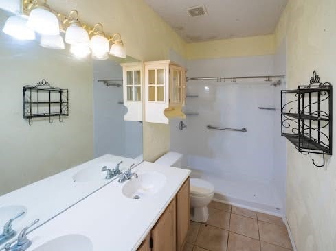 bathroom with walk in shower, a sink, tile patterned flooring, double vanity, and toilet
