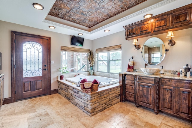 bathroom with a tray ceiling, recessed lighting, ornamental molding, a bath, and vanity