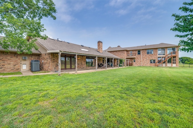 rear view of house featuring a patio, central air condition unit, a yard, a chimney, and brick siding