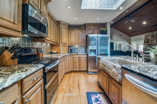 kitchen featuring light wood finished floors, light stone countertops, a sink, lofted ceiling with skylight, and appliances with stainless steel finishes