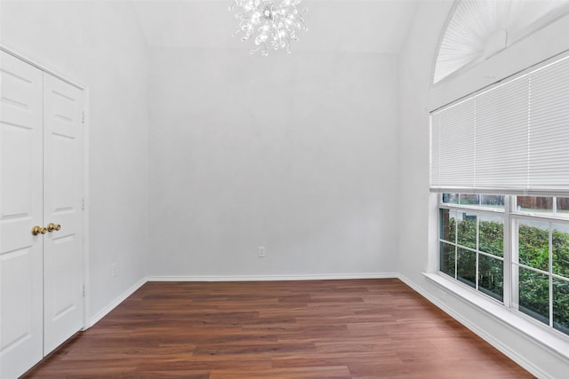 spare room featuring an inviting chandelier, wood finished floors, vaulted ceiling, and baseboards