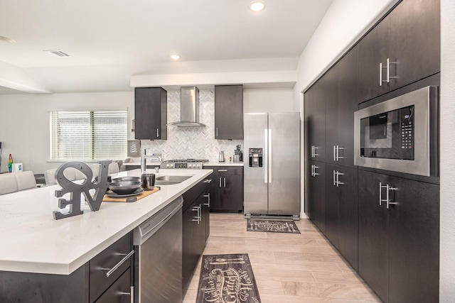 kitchen with a center island with sink, light countertops, wall chimney exhaust hood, a sink, and appliances with stainless steel finishes