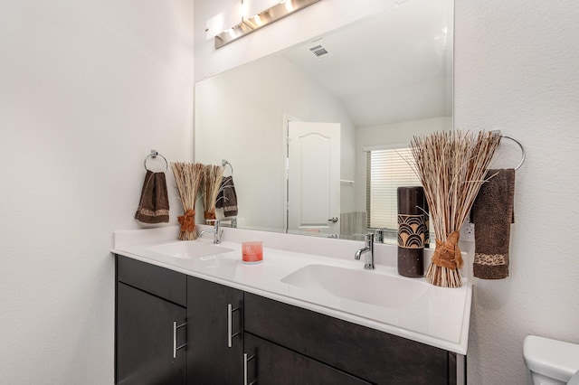 bathroom with a sink, toilet, double vanity, and lofted ceiling