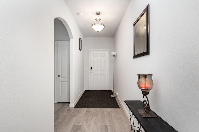 entryway with arched walkways, baseboards, and light wood-type flooring