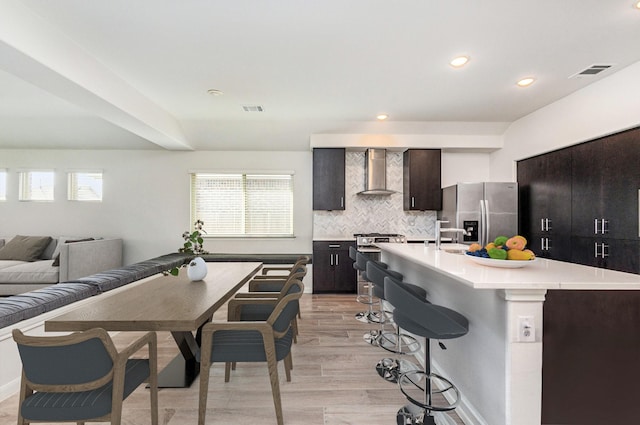 kitchen featuring wall chimney range hood, decorative backsplash, a breakfast bar area, light countertops, and stainless steel appliances