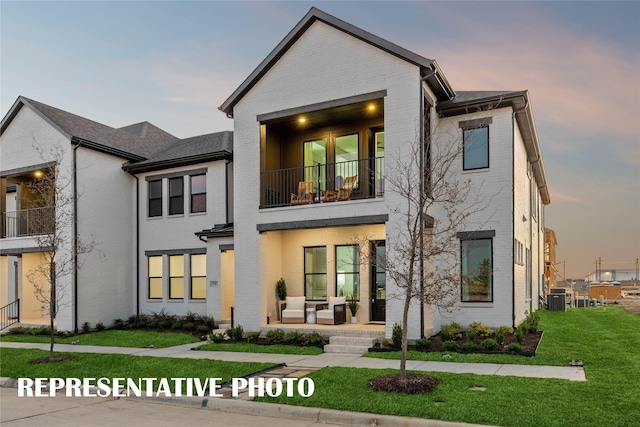 view of front of property with central air condition unit, a front yard, a balcony, and brick siding