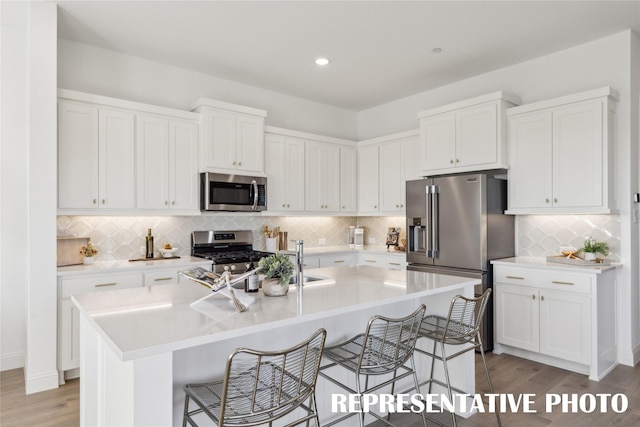 kitchen with appliances with stainless steel finishes, a breakfast bar area, white cabinetry, and backsplash