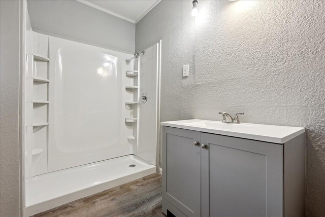 bathroom with walk in shower, vanity, a textured wall, and wood finished floors
