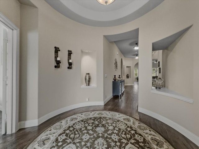 hall featuring arched walkways, baseboards, and wood finished floors