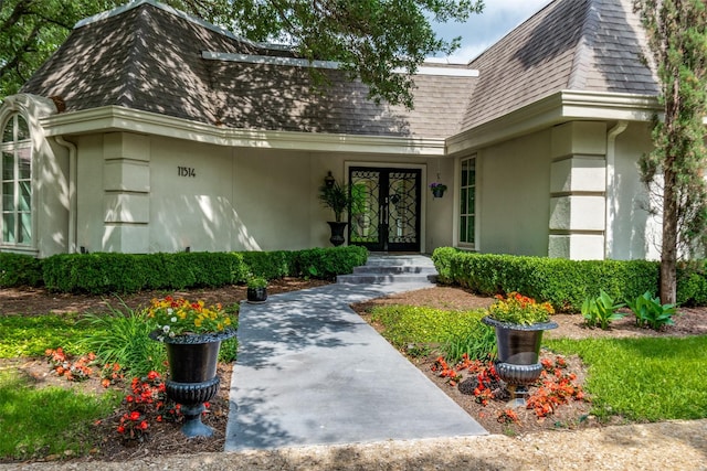 property entrance featuring roof with shingles, stucco siding, mansard roof, and french doors