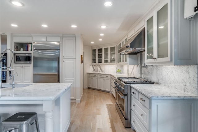 kitchen featuring built in appliances, white cabinetry, wall chimney exhaust hood, and light wood-type flooring