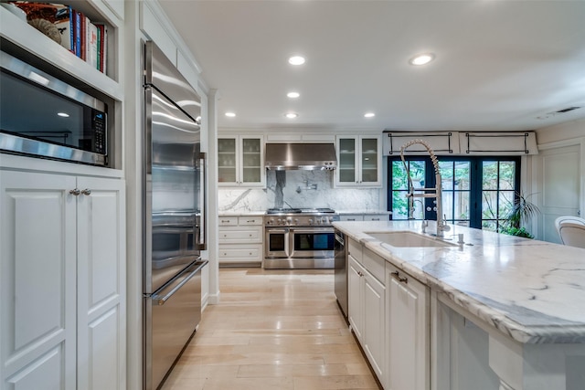 kitchen with decorative backsplash, high quality appliances, a sink, under cabinet range hood, and white cabinetry