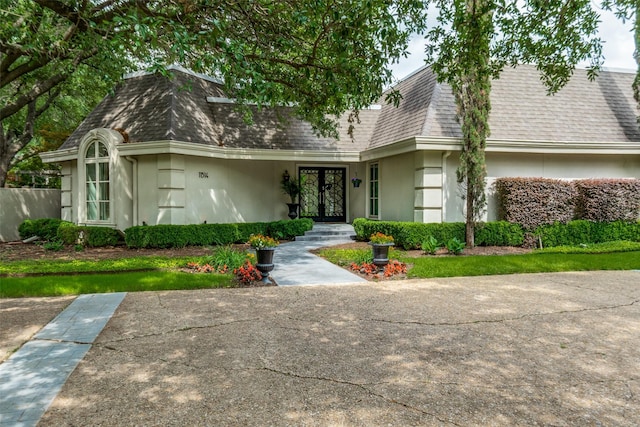 view of front facade with mansard roof, stucco siding, french doors, and roof with shingles
