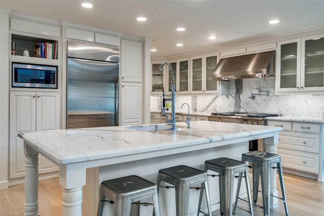 kitchen with built in appliances, white cabinetry, ventilation hood, and light wood finished floors