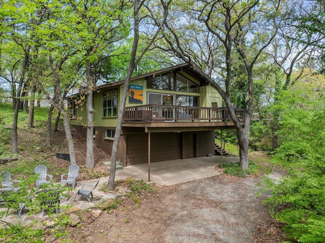 rear view of property featuring a wooden deck, stairs, a garage, and driveway