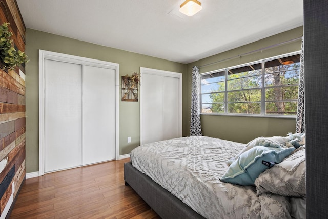 bedroom with baseboards, wood finished floors, and multiple closets