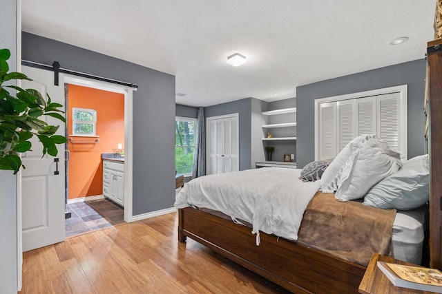 bedroom featuring light wood finished floors, multiple closets, a barn door, and ensuite bathroom