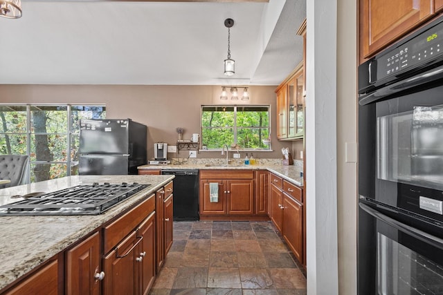 kitchen featuring brown cabinets, a sink, black appliances, light stone counters, and stone finish floor