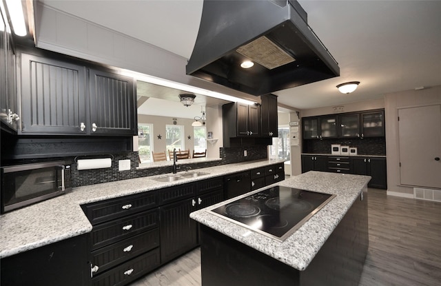 kitchen with black electric stovetop, decorative backsplash, stainless steel microwave, extractor fan, and a sink