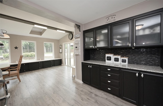 kitchen featuring light wood finished floors, vaulted ceiling, dark cabinetry, and tasteful backsplash