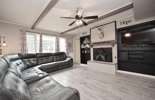 living area featuring light wood-style floors, built in shelves, a brick fireplace, beam ceiling, and a ceiling fan