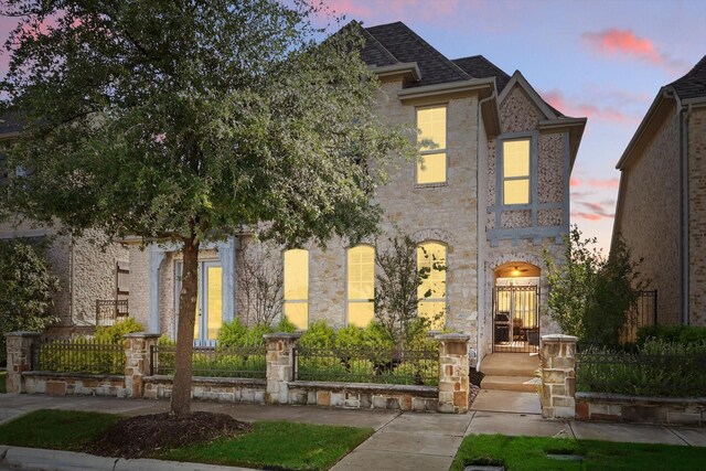 french country style house with a fenced front yard and stone siding