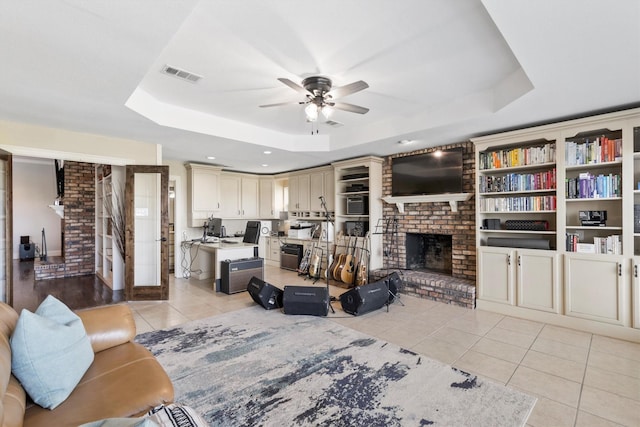living area with light tile patterned floors, visible vents, ceiling fan, a tray ceiling, and a fireplace
