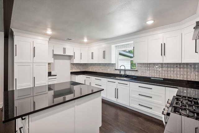 kitchen featuring white cabinets, stainless steel gas range oven, a sink, backsplash, and visible vents
