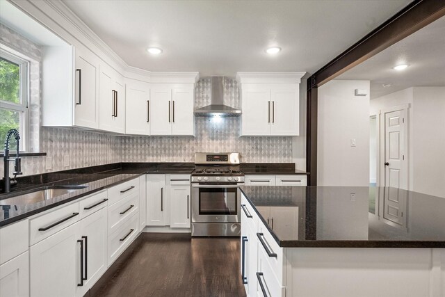kitchen with wall chimney range hood, stainless steel gas range oven, a sink, white cabinets, and dark wood-type flooring