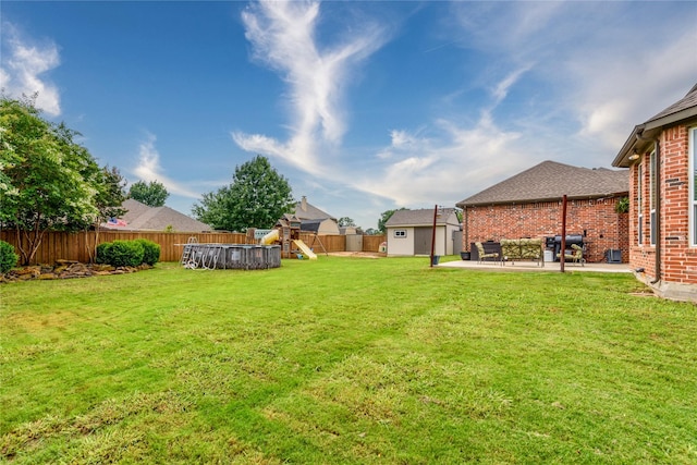 view of yard with a patio, an outbuilding, a fenced backyard, a playground, and a storage unit
