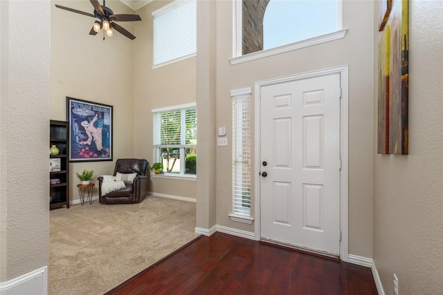 entryway featuring a towering ceiling, wood finished floors, ceiling fan, and baseboards