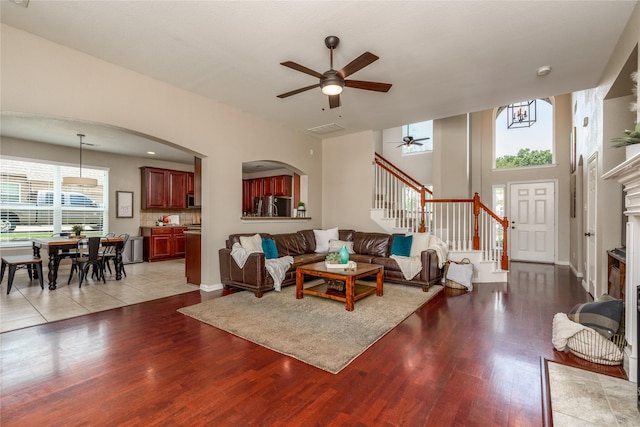 living room featuring wood finished floors, arched walkways, stairs, visible vents, and a ceiling fan
