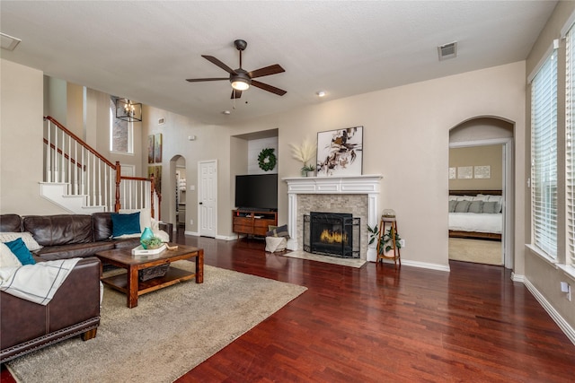 living area with wood finished floors, arched walkways, stairs, a ceiling fan, and a fireplace with flush hearth