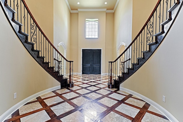 foyer entrance with baseboards, stairway, ornamental molding, and a towering ceiling