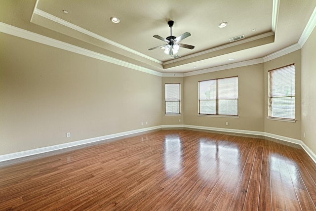 empty room featuring ceiling fan, a raised ceiling, visible vents, ornamental molding, and wood finished floors
