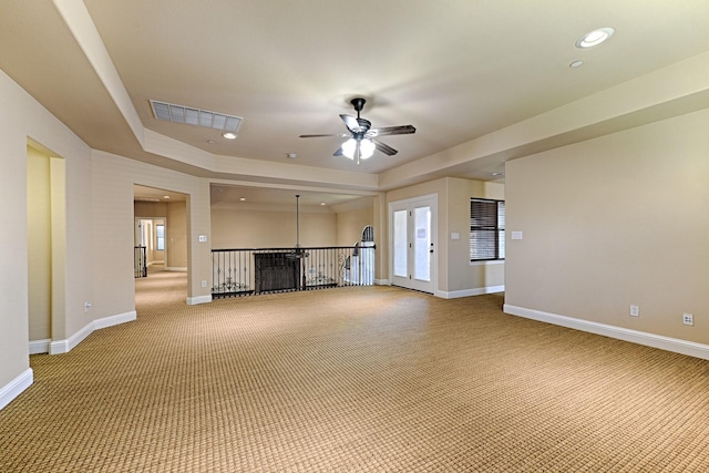 unfurnished living room with light colored carpet, visible vents, ceiling fan, a tray ceiling, and baseboards