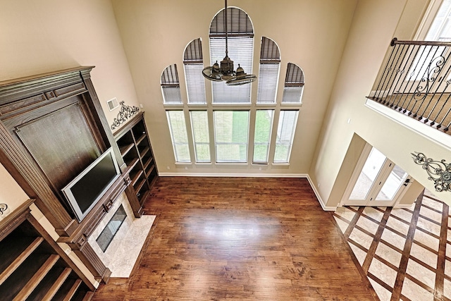 unfurnished living room with baseboards, wood finished floors, a chandelier, and a high ceiling