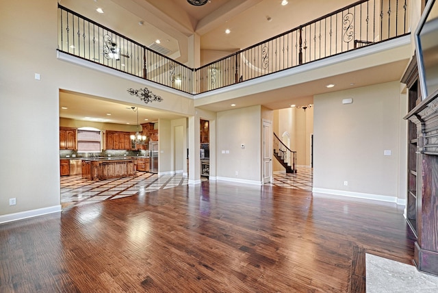 unfurnished living room with stairway, an inviting chandelier, dark wood finished floors, a fireplace, and a towering ceiling