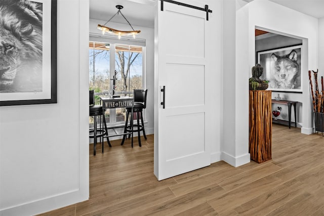 hall featuring light wood finished floors, a barn door, and baseboards