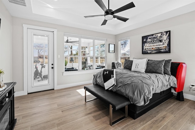 bedroom with light wood finished floors, access to outside, a raised ceiling, visible vents, and baseboards