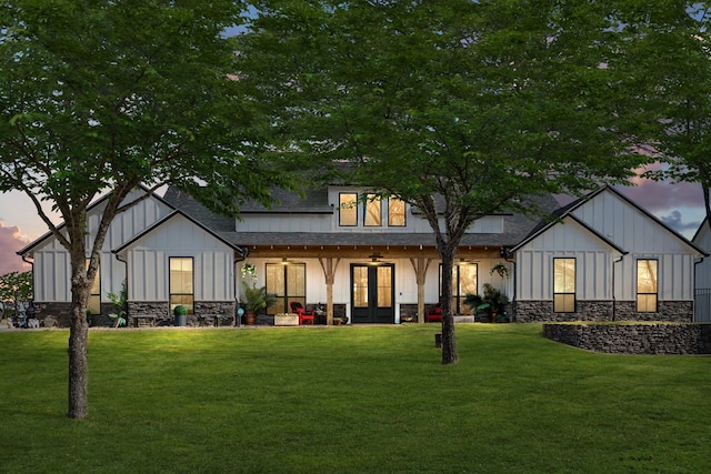 back of property at dusk featuring board and batten siding, a yard, ceiling fan, and stone siding