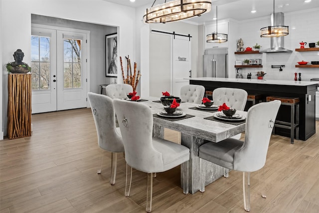 dining area with a barn door, recessed lighting, and light wood-style floors