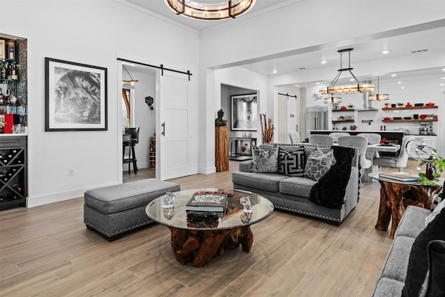 living room featuring crown molding, light wood finished floors, a barn door, and baseboards