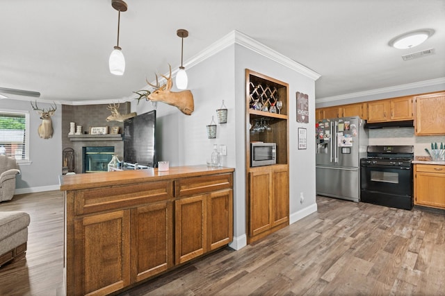 kitchen with wood finished floors, stainless steel appliances, a fireplace, open floor plan, and crown molding